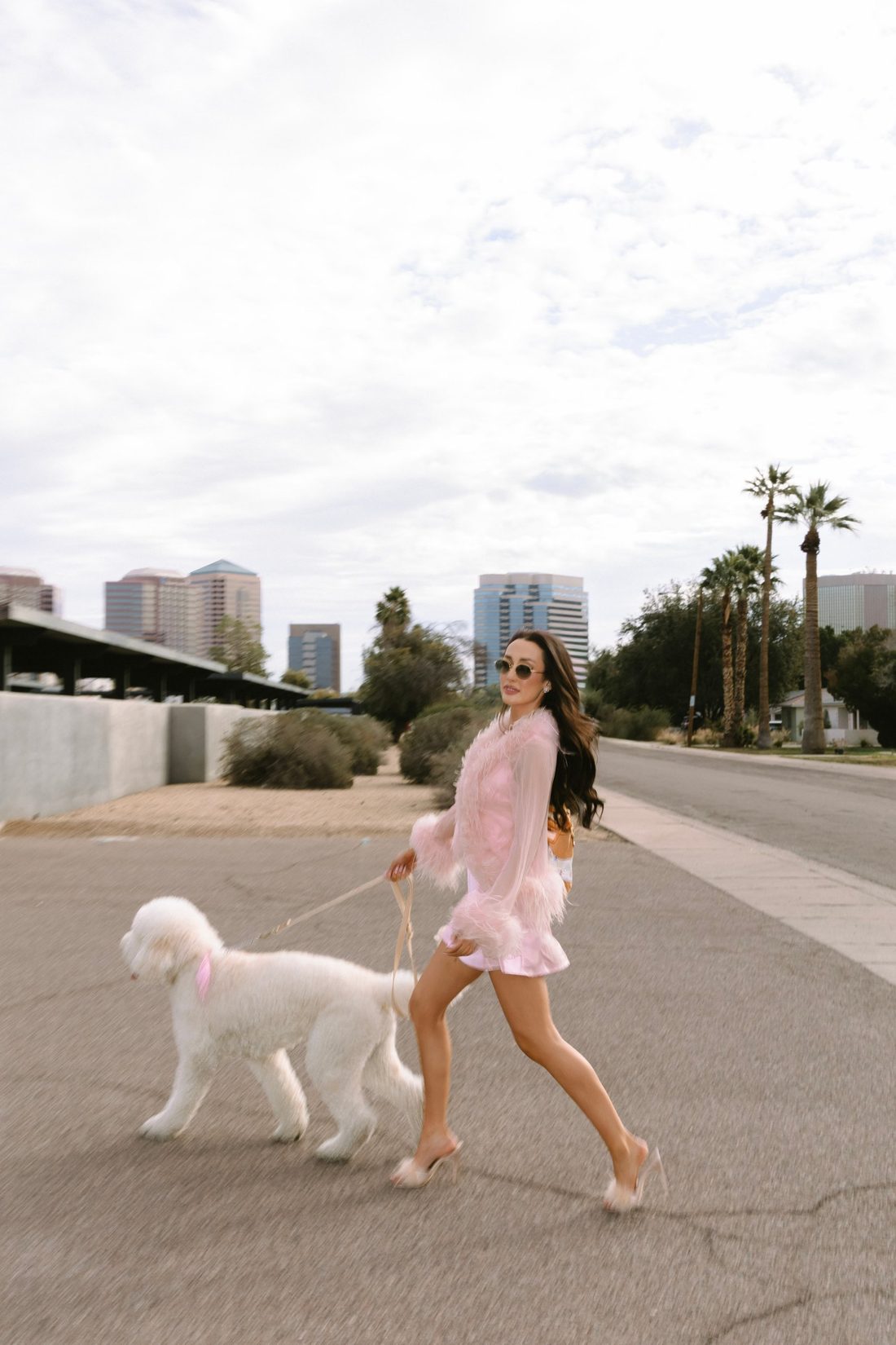 Mackenzie Kern in pink feathers walking her white doodle, Leo, through the city