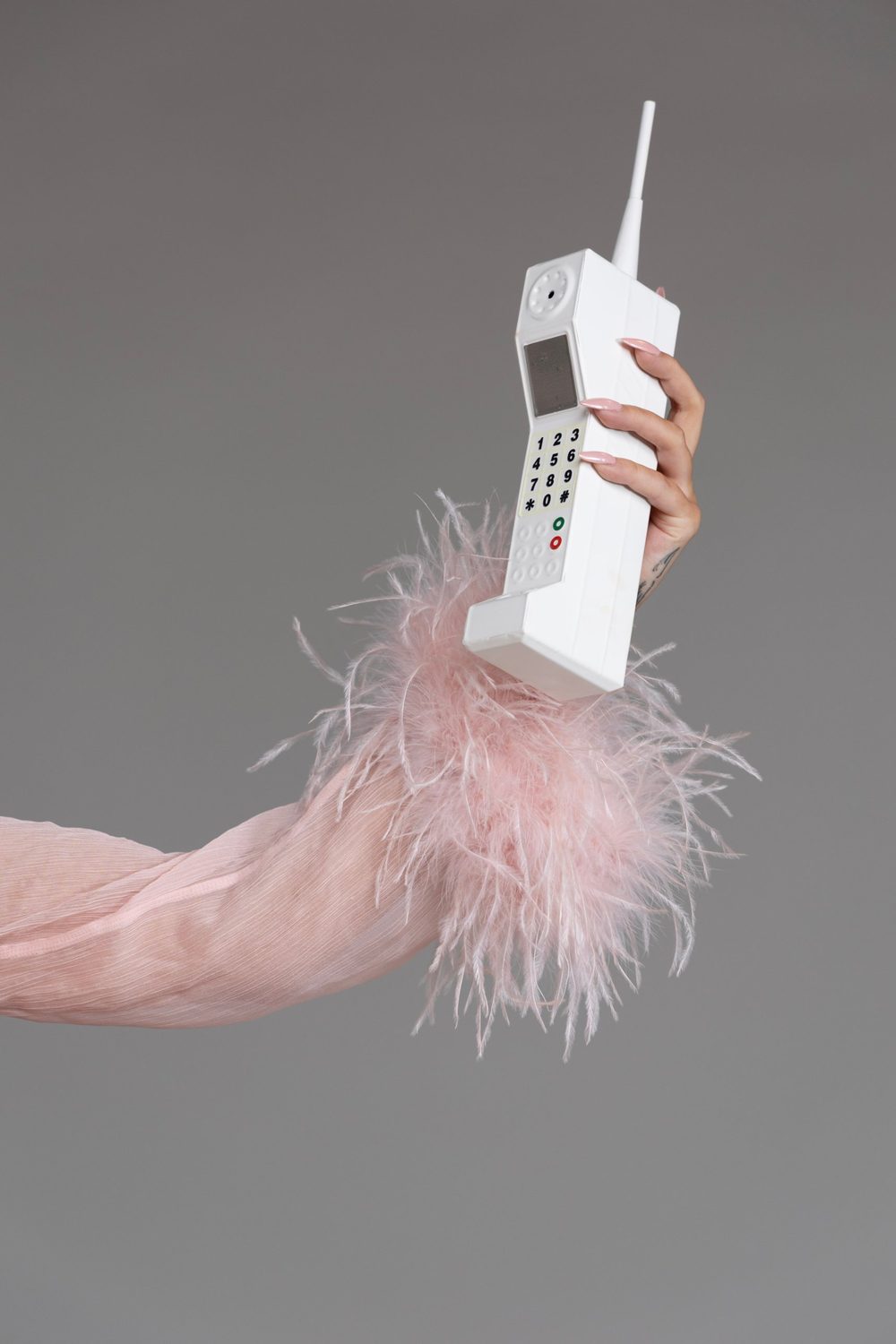 A hand with pink feather cuff holding a white vintage cell phone